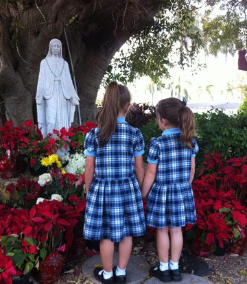 Two young girls standing in front of a statue of mary praying