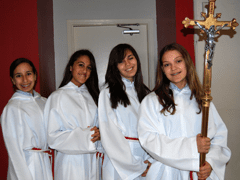 Four girls, one holding cross, all wearing albs ready to serve at Mass